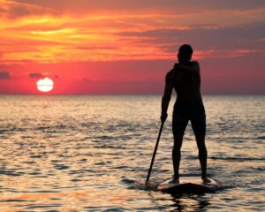 person on paddleboard riding into sunset