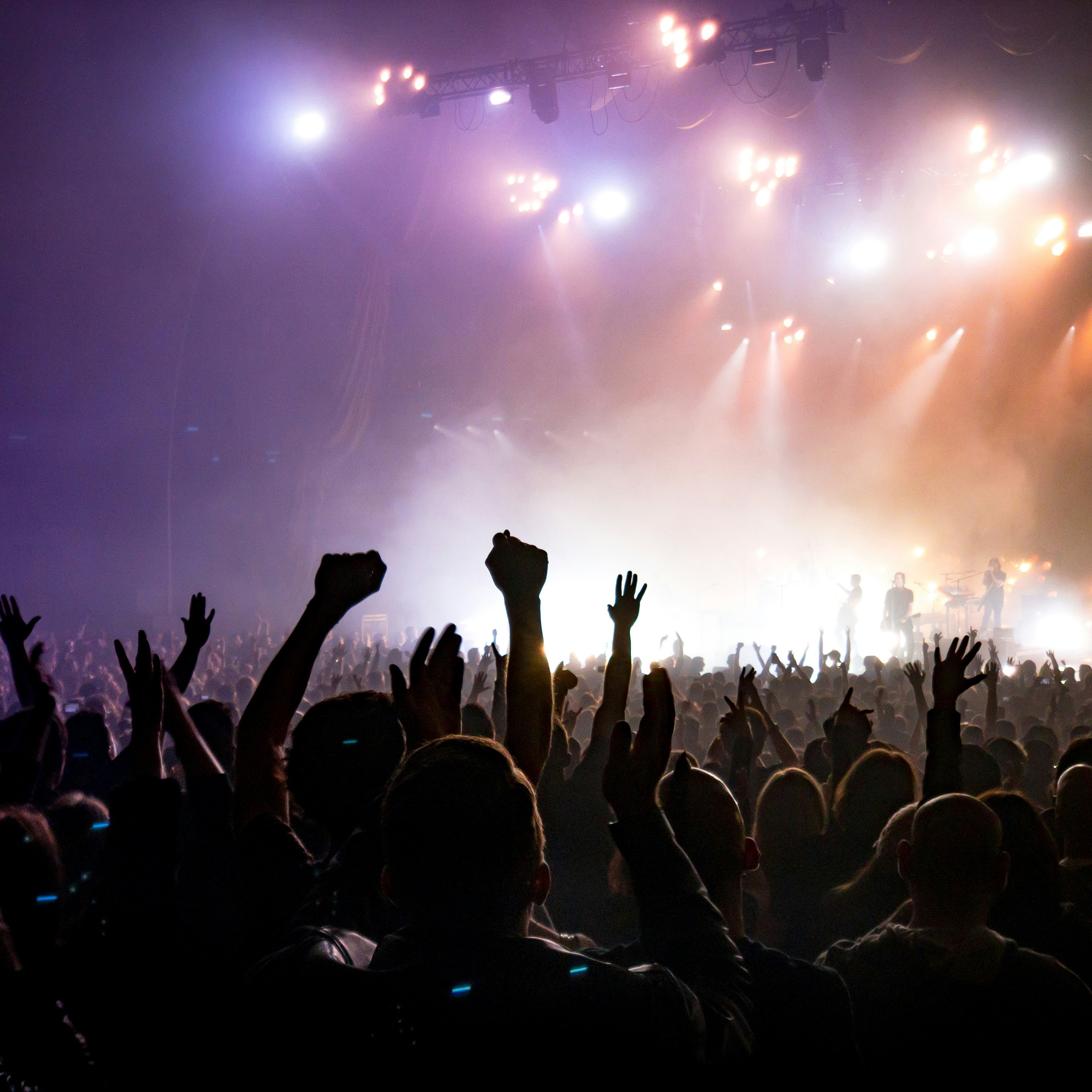 people waving arms in air enthusiastically at concert with lights flashing from the stage