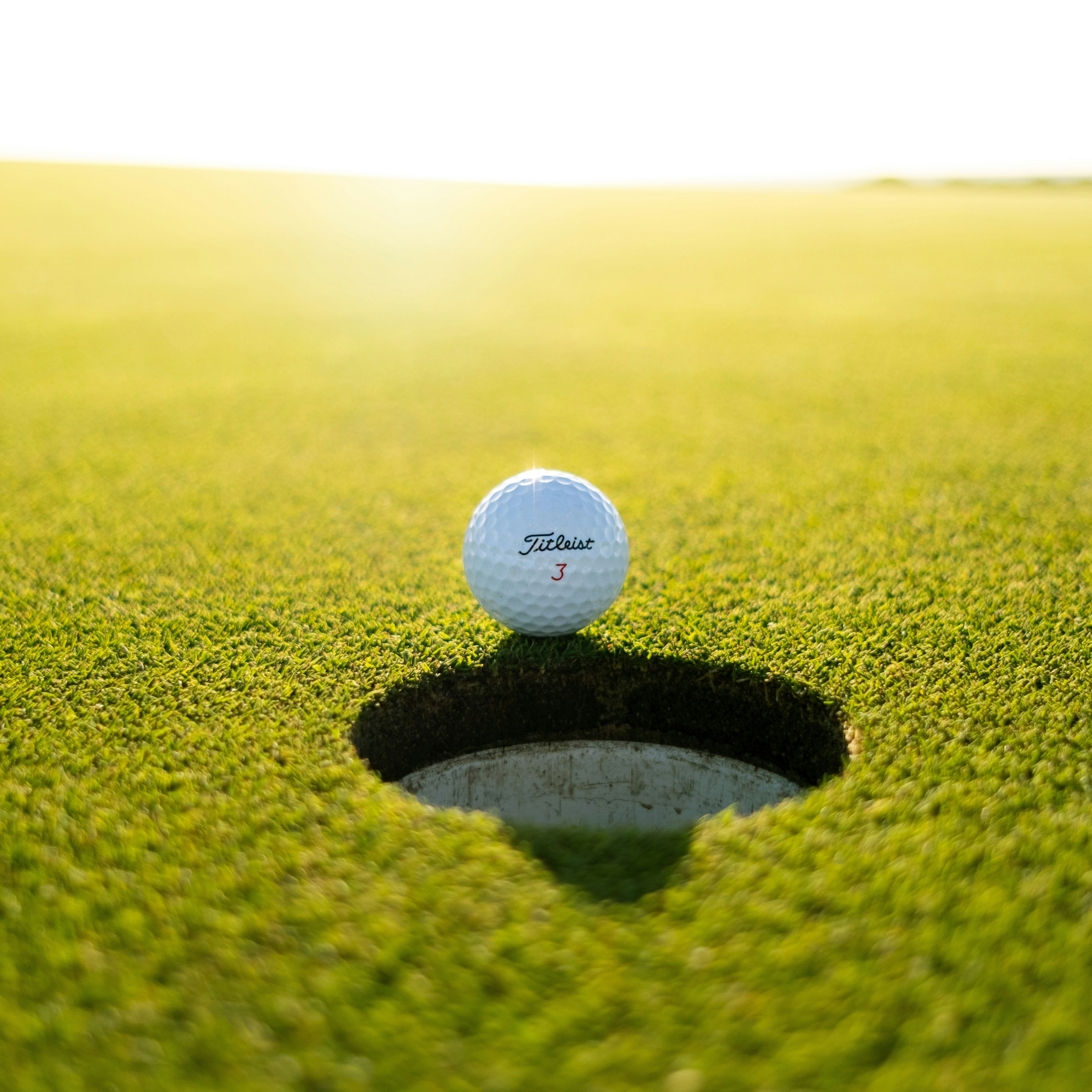 golf ball on green grass about to fall into hole
